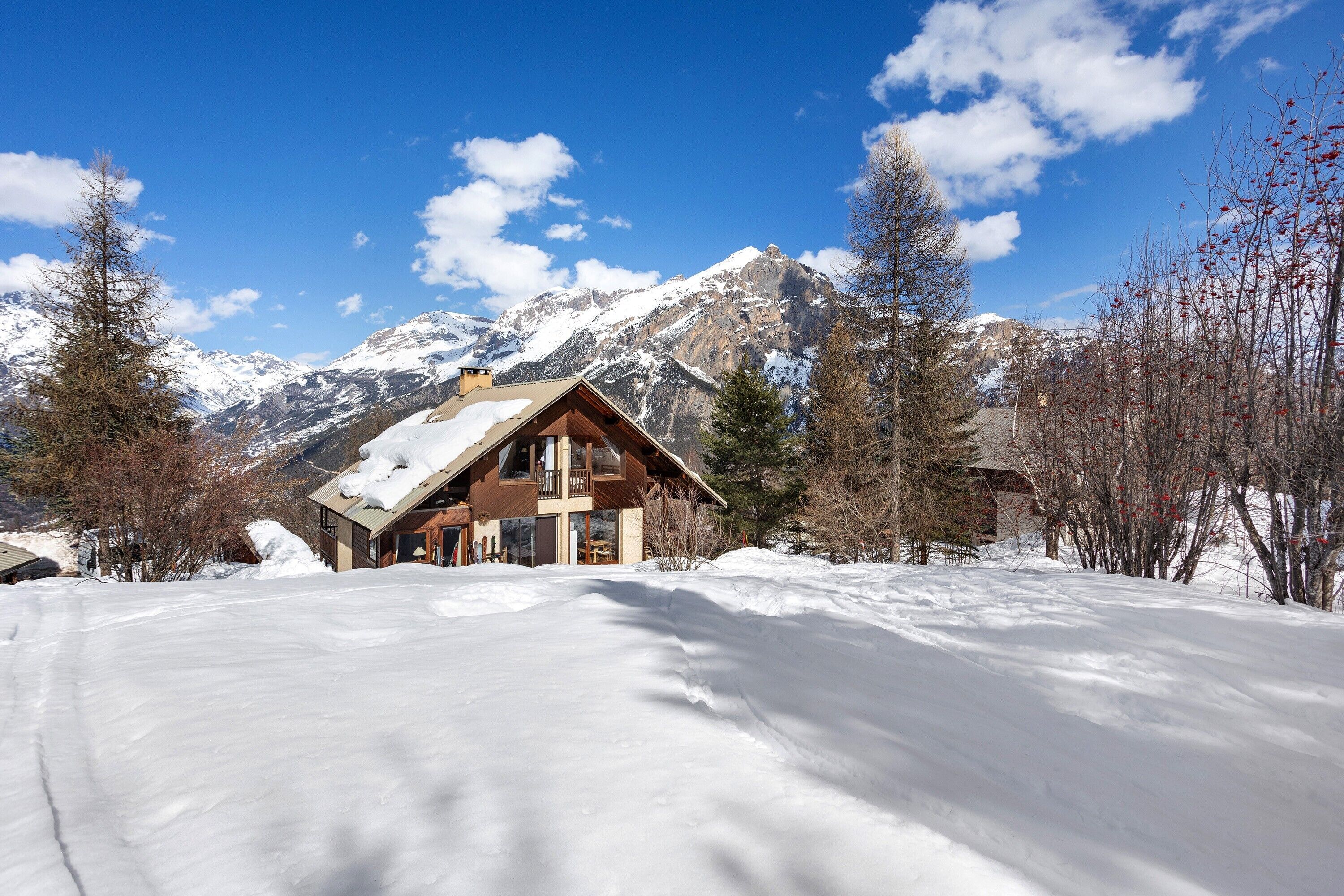 Eine Holzhütte mit geneigtem Dach, umgeben von schneebedecktem Boden und Bergen im Hintergrund.