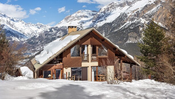 A wooden chalet with a balcony, surrounded by snow-covered mountains.