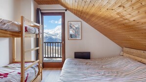 A room with a bunk bed, a desk, a window with a view of mountains, and a wooden ceiling.
