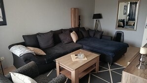 Un saló modern amb un sofà de color fosc, una taula de centre de fusta i un llit amb llençol blau.