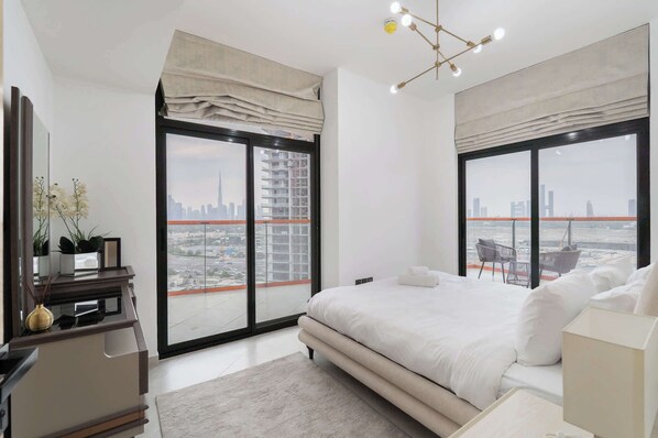 A modern bedroom with a large bed, a desk, and a chair. There are two large windows with city views. - Stayshort - Magnificent 3 Bedroom Apartment in Al Jaddaf That Sleeps 8 (Dubai)