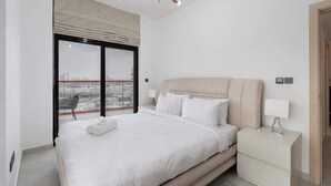 A bedroom with a large bed, a nightstand, a lamp, and a view of the city through floor-to-ceiling windows. - Stayshort - Magnificent 3 Bedroom Apartment in Al Jaddaf That Sleeps 8 (Dubai)