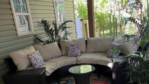 A covered outdoor seating area with a curved sofa, wicker chairs, and a patterned rug. - 3-bedroom  house in welcoming Garner with cool BAMBOO for relaxing stays (Garner)