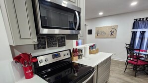 A modern kitchen with stainless steel appliances, a microwave, and a stove. There are cabinets, a countertop, and a dining area with a table and chairs. - 3-bedroom  house in welcoming Garner with cool BAMBOO for relaxing stays (Garner)