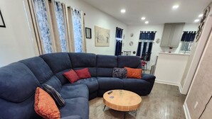 A modern living room with a dark blue sectional sofa, two round wooden coffee tables, and a kitchen area in the background. - 3-bedroom  house in welcoming Garner with cool BAMBOO for relaxing stays (Garner)