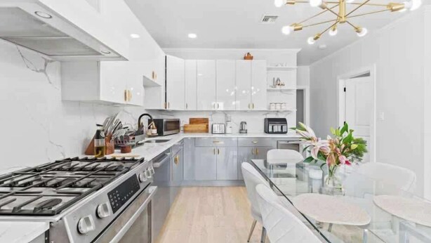 A modern kitchen with white cabinets, stainless steel appliances, and a glass dining table.