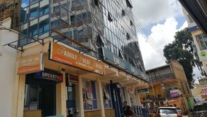 Een meerhoog gebouw met een glazen gevel, een bordje voor een familiepension en diverse winkels, waaronder een bank en een restaurant.
