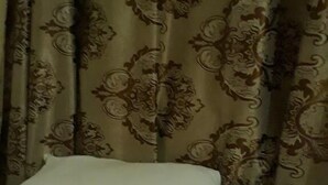 Een bed met witte kussens en een gestreept beddegoed, een gordijn met een bloemenprint en een houten vloer.