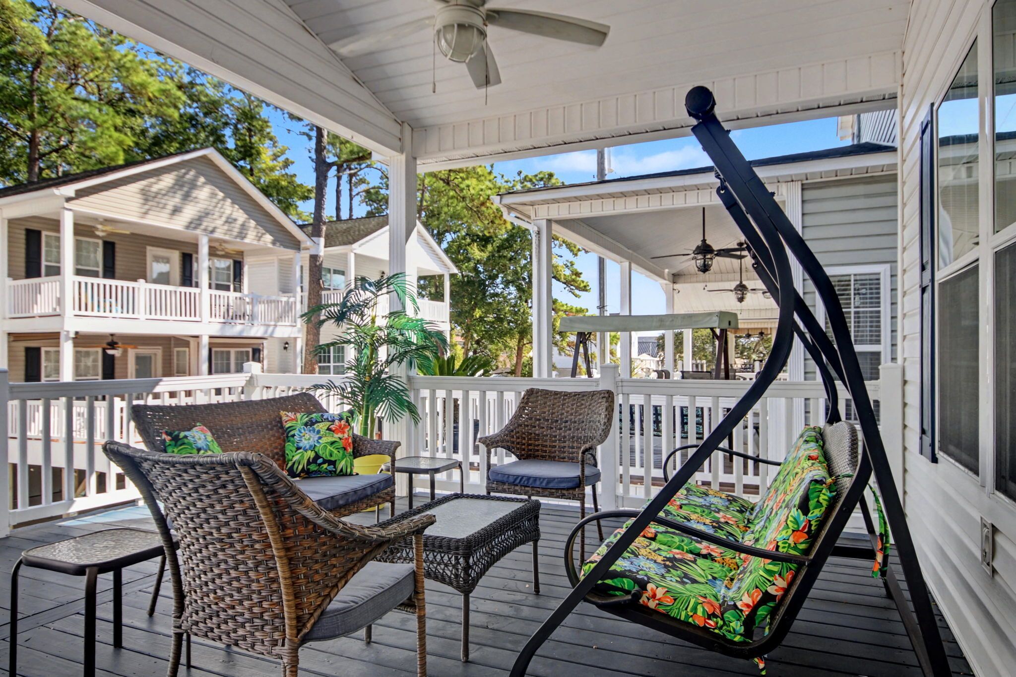 A covered porch with wicker furniture, a ceiling fan, and a view of neighboring buildings.