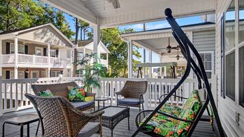 A covered porch with wicker furniture, a ceiling fan, and a view of neighboring buildings.