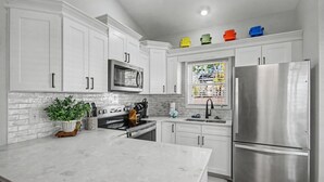 A modern kitchen with white cabinetry, a stainless steel refrigerator, and a large island. - The Surf Shack-Limo Golf Cart & Linens Included in Ocean Lakes Family Campground (Myrtle Beach)