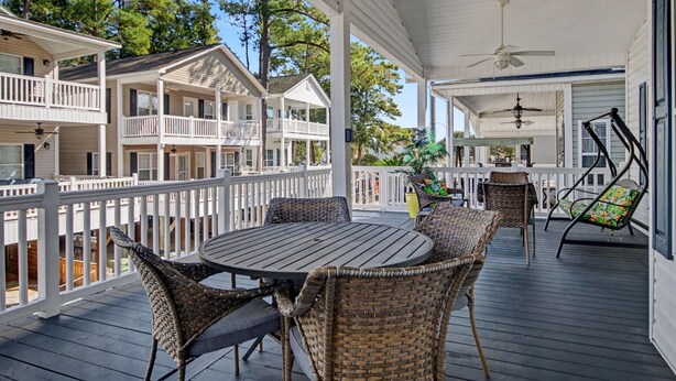 A covered outdoor deck with wicker furniture, a round table, and a ceiling fan. - The Surf Shack-Limo Golf Cart & Linens Included in Ocean Lakes Family Campground (Myrtle Beach)
