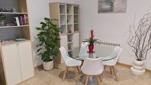 Uma sala de jantar com mesa de vidro, cadeiras brancas, um vaso de planta e um armário com portas de vidro.