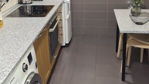 Cozinha compacta com micro-ondas, fogão, geladeira e máquina de lavar. Um relógio está na parede e uma planta em cima da mesa.