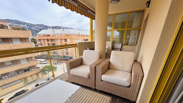 Un balcón con mobiliario de mimbre y vistas a edificios y montañas.