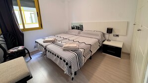 Un dormitorio ordenado con cama, mesita de noche, lámpara y sillón.