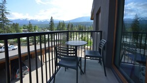 Un balcon avec une table et des chaises, d’où l’on peut admirer un parking et des montagnes au loin.