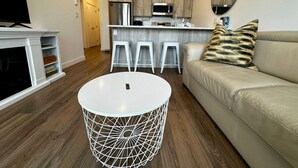 Un salon moderne avec une table ronde blanche, un canapé beige et un coin cuisine à l’arrière-plan.