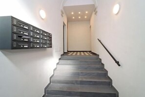 A staircase with a handrail, a wall-mounted storage unit, and recessed lighting. - Abode Queen In The Fortress (Florence)
