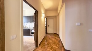 A hallway with a herringbone-patterned wooden floor, a kitchen visible through an open door, and a light switch on the wall. - Luxury Apartment Palazzo Vecchio with view (Firenze)
