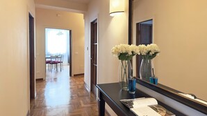 A hallway with a wooden floor, a dining area in the background, and a table with chairs. There are two vases with flowers on a console table. - Luxury Apartment Palazzo Vecchio with view (Firenze)