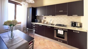 A modern kitchen with dark cabinetry, a gas stove, a microwave, and a coffee maker. There is a dining table with chairs and a vase of flowers. - Luxury Apartment Palazzo Vecchio with view (Firenze)
