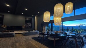 Una sala de estar moderna con un televisor grande, asientos cómodos y ventanas amplias con vistas al exterior.