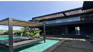 Un área de piscina moderna al aire libre con una pérgola, una tumbona y un camino de piedra.
