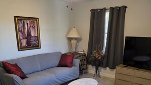 A living room with a sofa, a coffee table, a TV, a ceiling fan, a lamp, and a painting on the wall. - Clean, Spacious, 3BR 1.5BA, Near Shipyards, Chevron, Beach, Casinos, Fenced yard (Pascagoula)