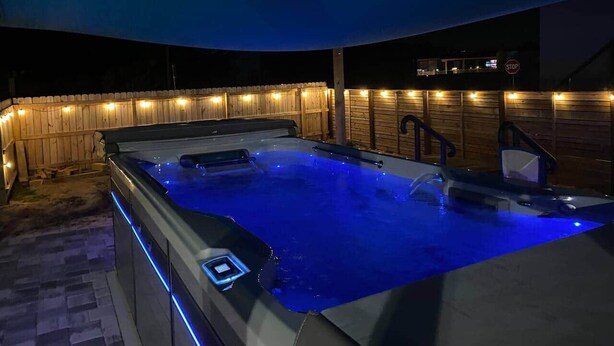 An outdoor hot tub with a wooden deck and string lights. - Cornerstone House (St. Augustine)