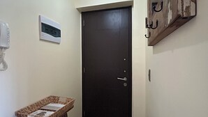 A hallway with a dark door, a light switch, a thermostat, and a telephone. - Departamento Bellavista (Osorno)