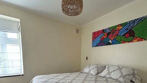 A bedroom with a bed, a window, a wall-mounted artwork, and a ceiling light fixture. - Departamento Bellavista (Osorno)