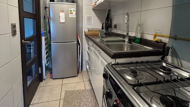 A compact kitchen with a refrigerator, microwave, stove, and sink. - Departamento Bellavista (Osorno)