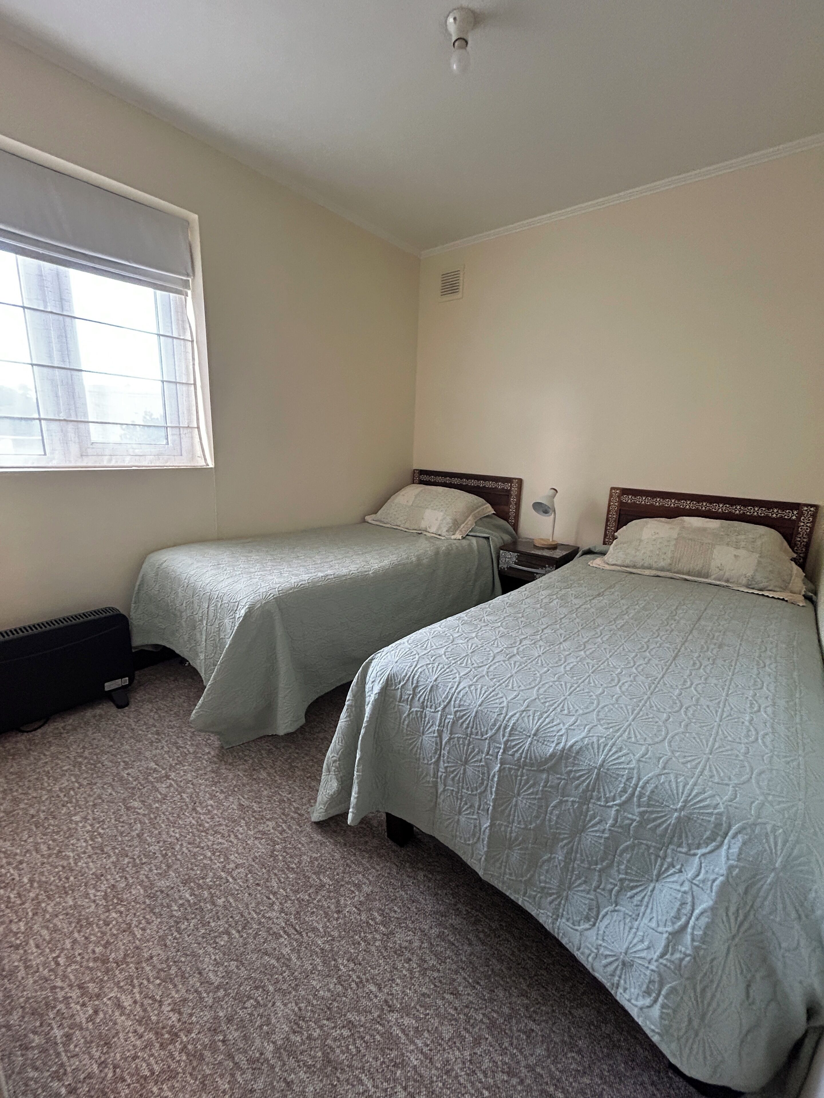 Une chambre avec deux lits simples, un radiateur et une fenêtre avec des stores.