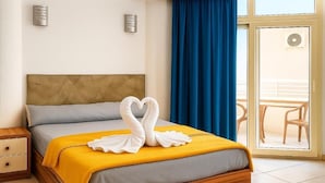 Habitación de hotel con cama, mesita de noche, ventana con cortinas azules y vistas al balcón exterior.