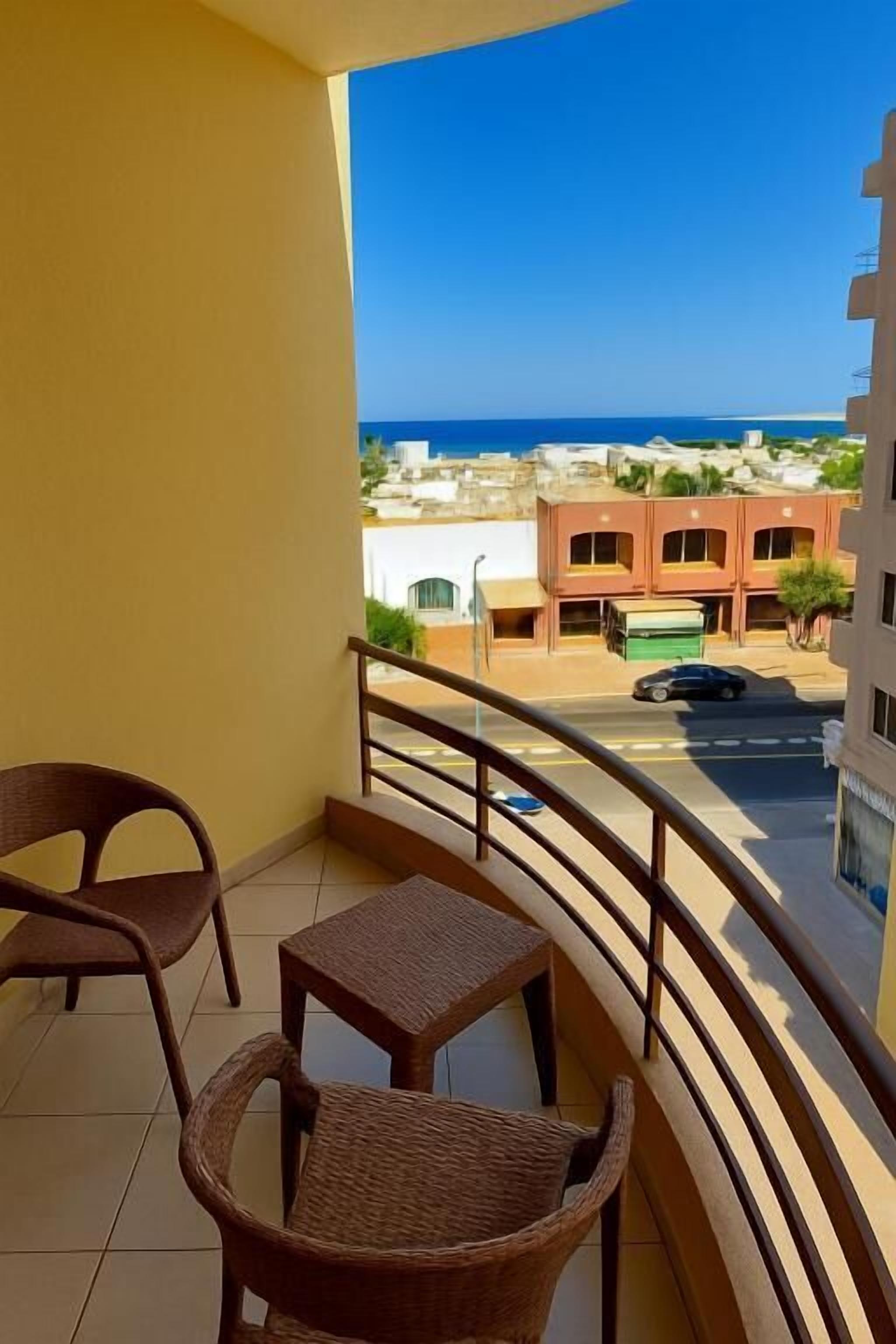A balcony with wicker furniture and a view of the sea and buildings.