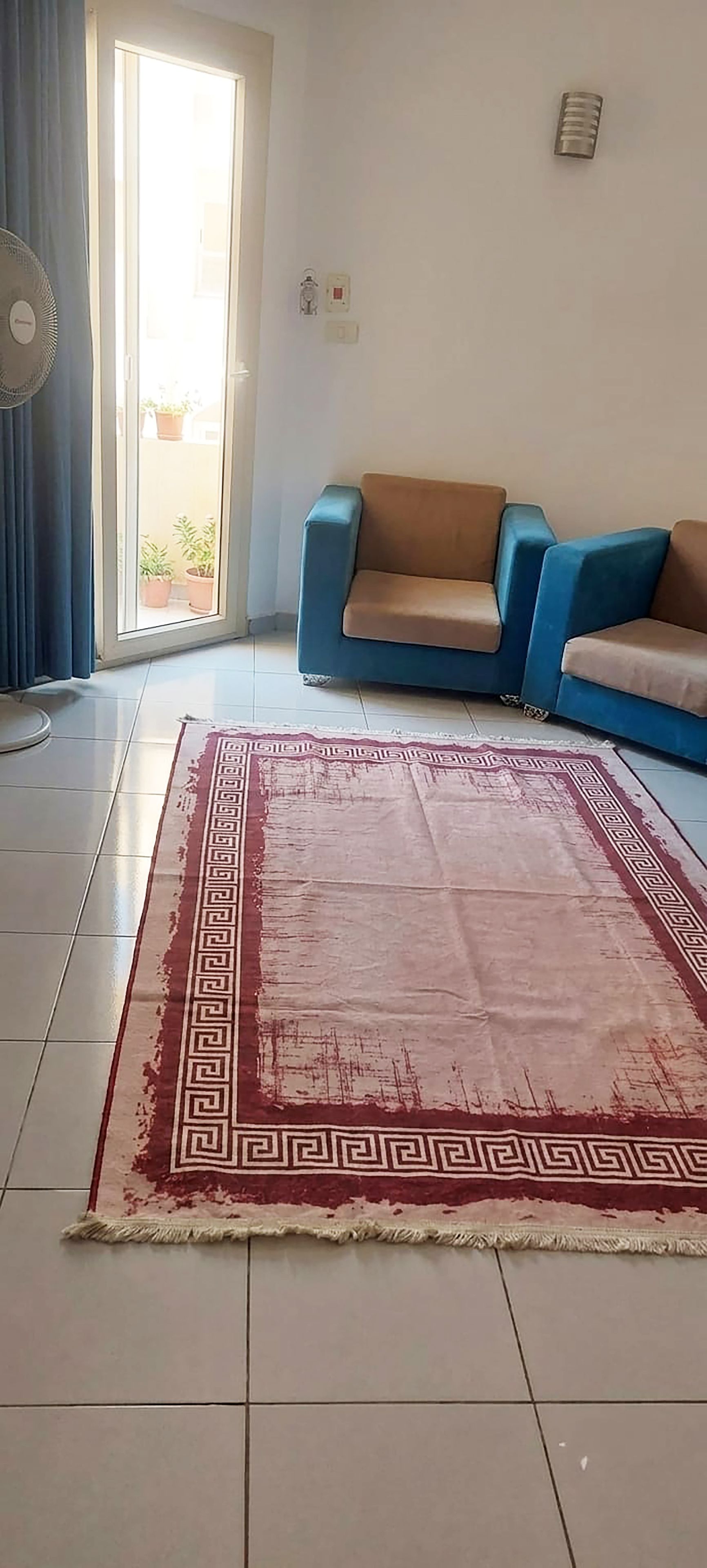 Een woonkamer met een blauwe bank, een kamerbreed tapijt met een patroon en een ventilator.