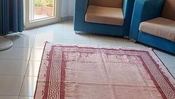 Een woonkamer met een blauwe bank, een kamerbreed tapijt met een patroon en een ventilator.
