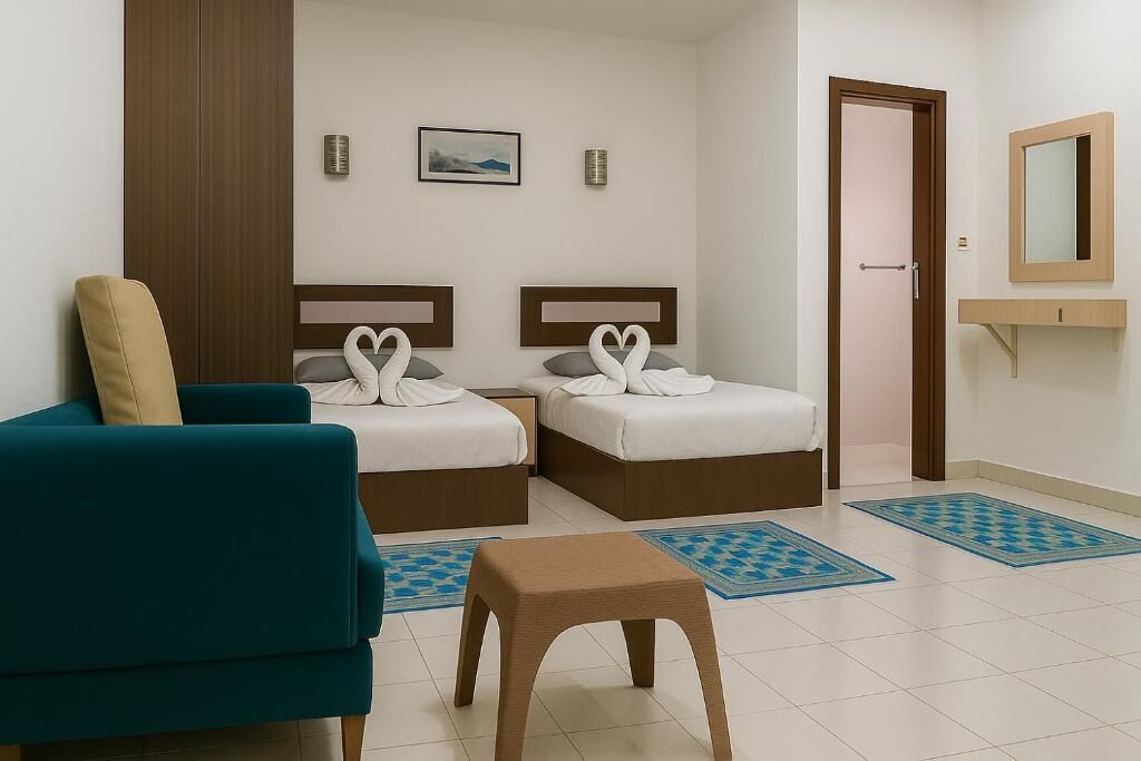 A hotel room with two beds, a sofa, a small table, and a bathroom with a mirror.