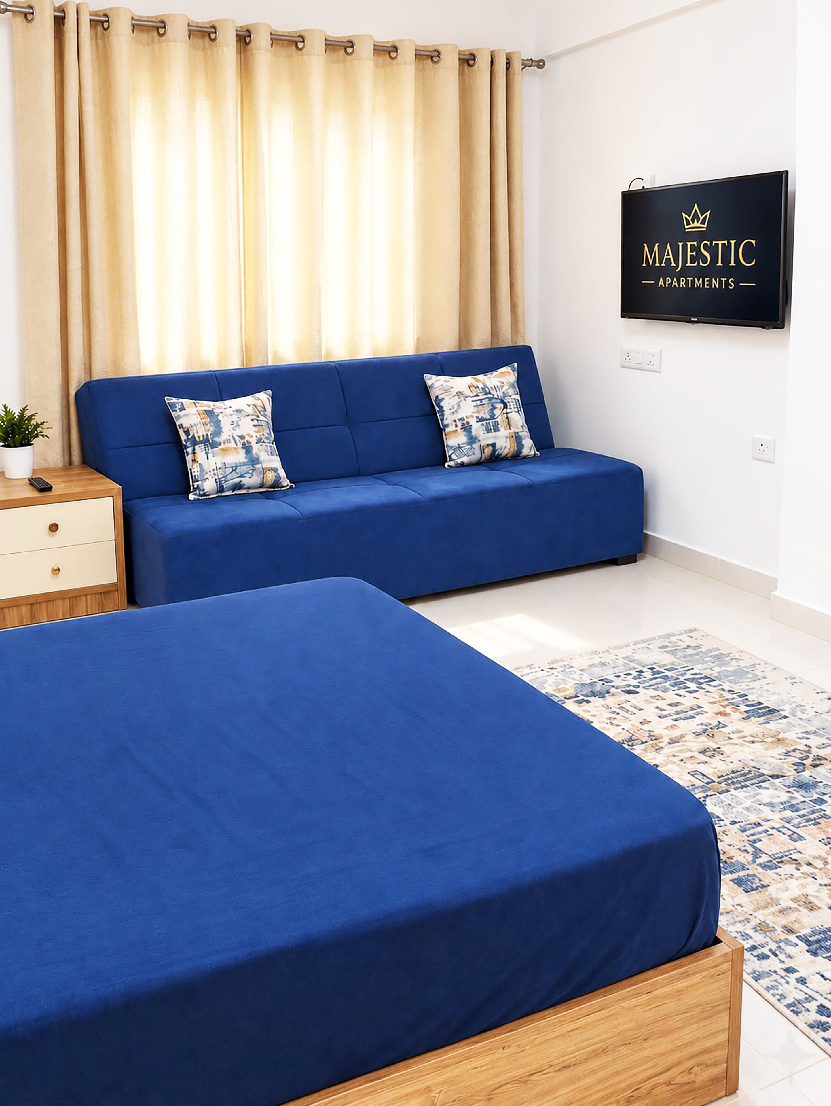 Un dormitori amb un sofà blau, dos llits, una catifa amb dibuixos i un cartell de Majestic Apartments.
