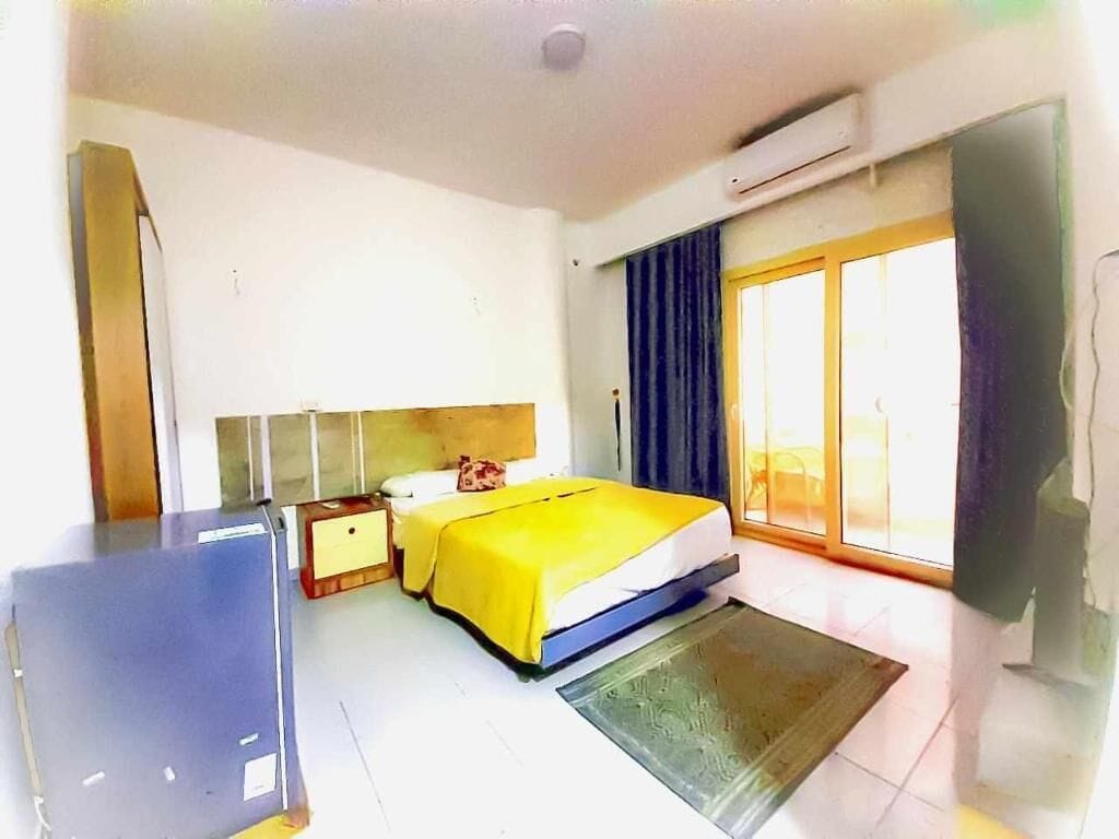 Une chambre d’hôtel avec un lit, un bureau, une chaise, une armoire et une fenêtre avec des rideaux.