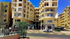 Un edificio residencial de varios pisos con balcones, una calle pavimentada y un cielo azul despejado.