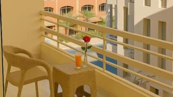 A balcony with two wicker chairs and a small table, overlooking a beach and other buildings.