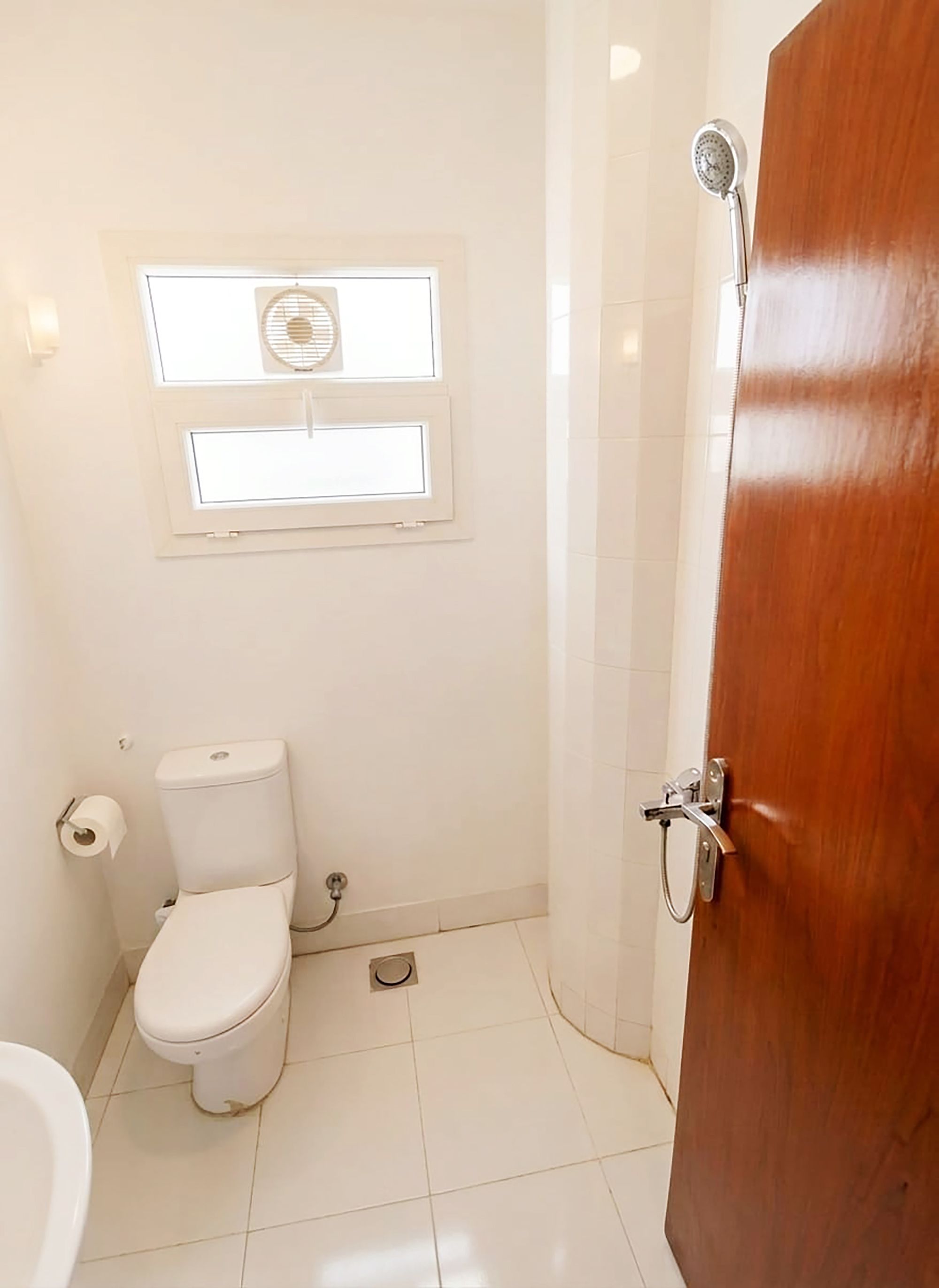 A small bathroom with a toilet, a window, and a shower.