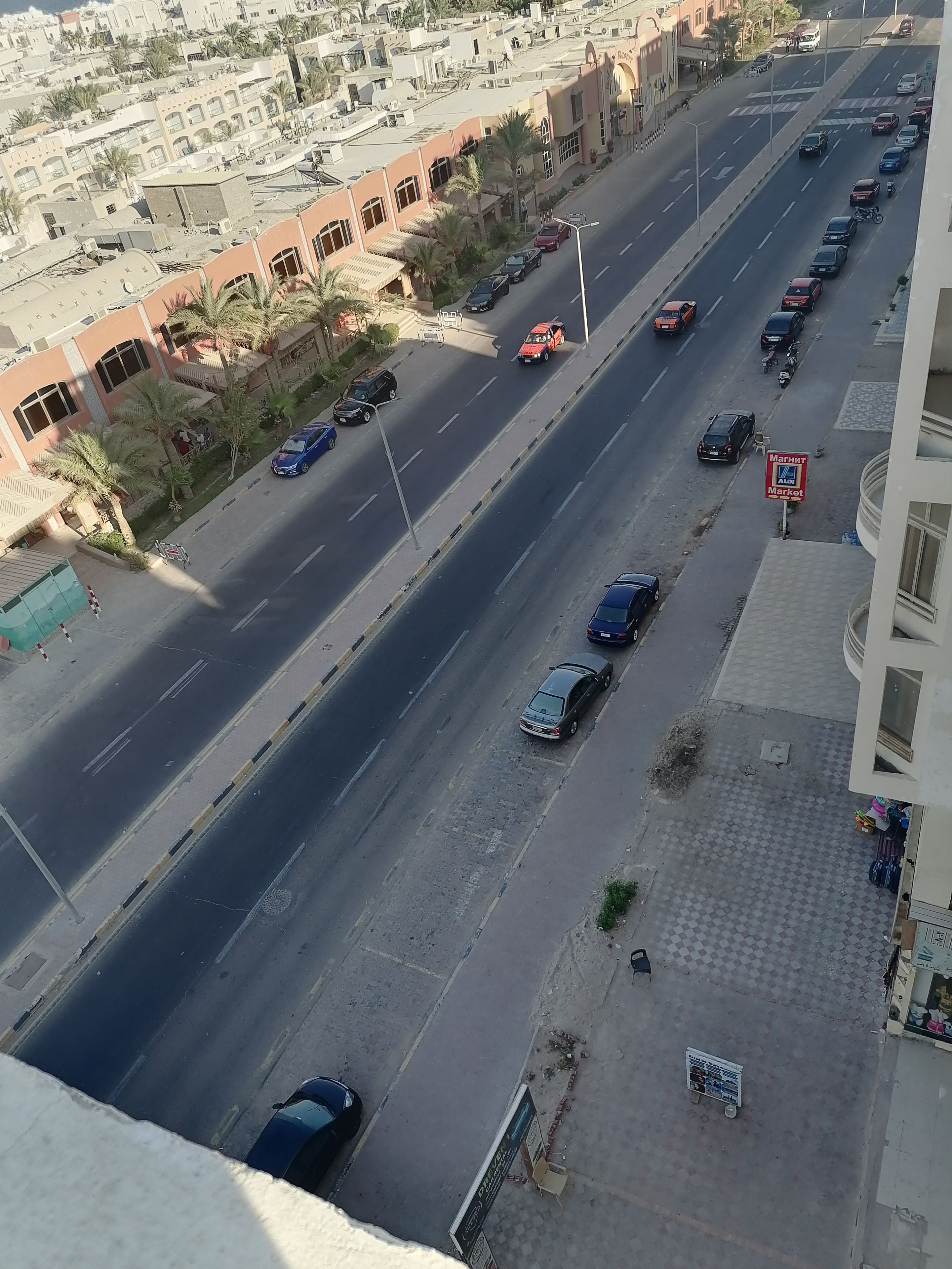 Una carretera con varios carriles, automóviles estacionados, un paso de peatones y un edificio con un letrero de mercado.