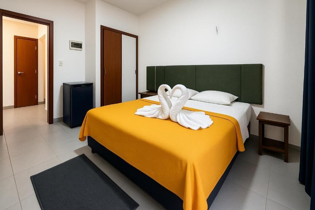 Ein Hotelzimmer mit Bett, Nachttisch, Mülleimer und einer Tür.