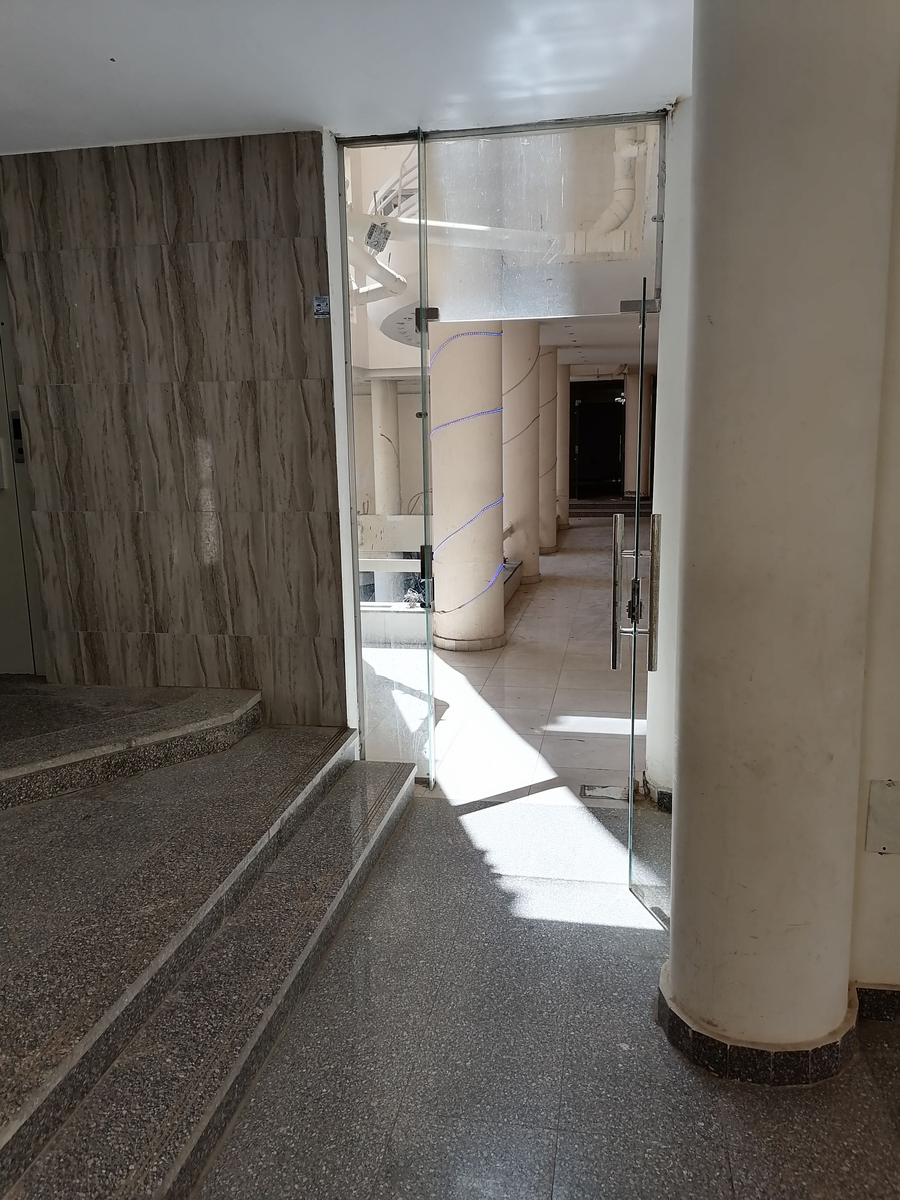 A hallway with marble walls and a glass door leading to a stairway.
