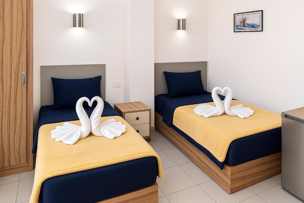 Two double beds with matching blue headboards and yellow bedspreads, each adorned with white swan-shaped towels.