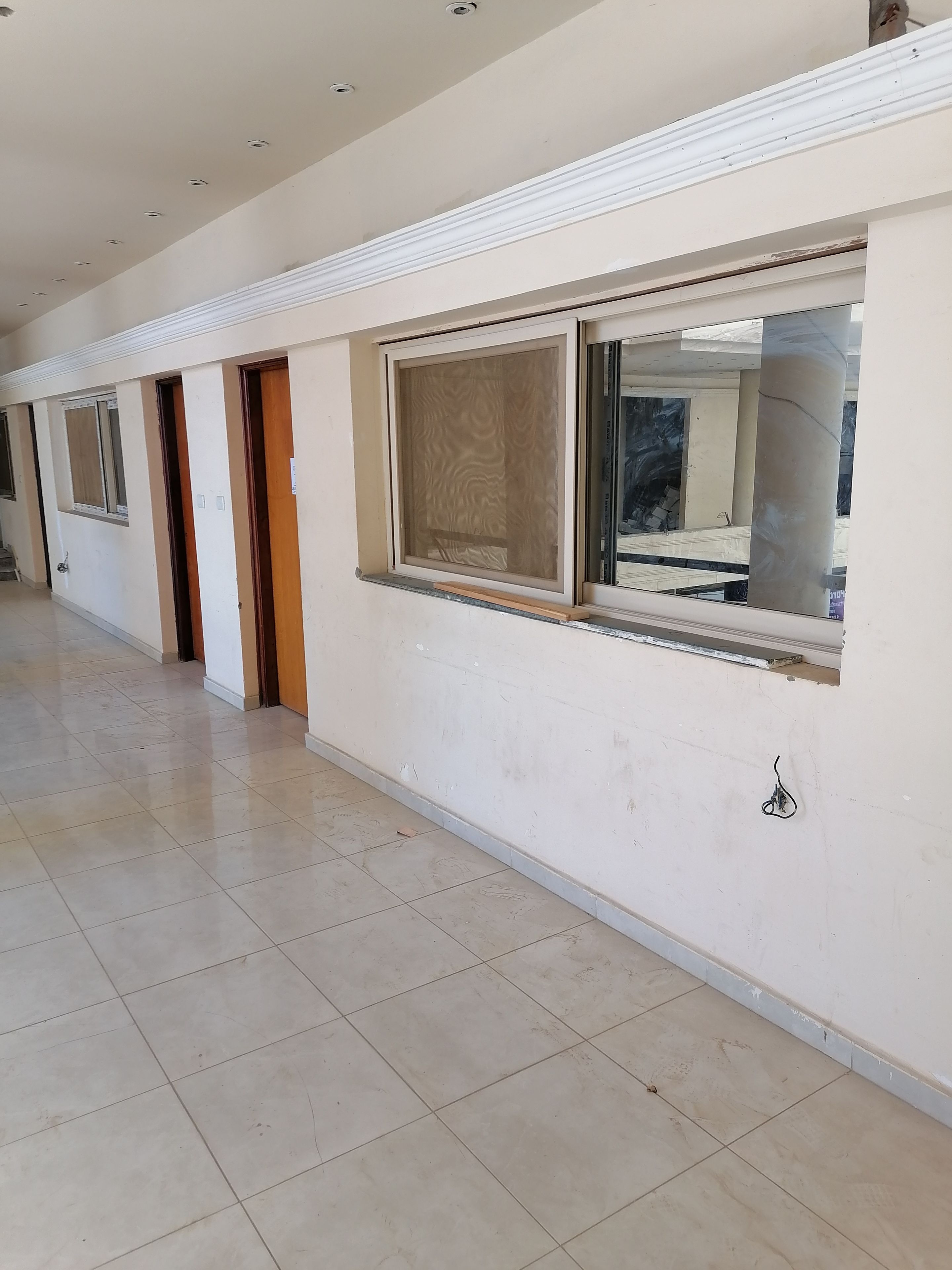 A corridor with multiple doors and windows, tiled floors, and a ceiling with recessed lighting.