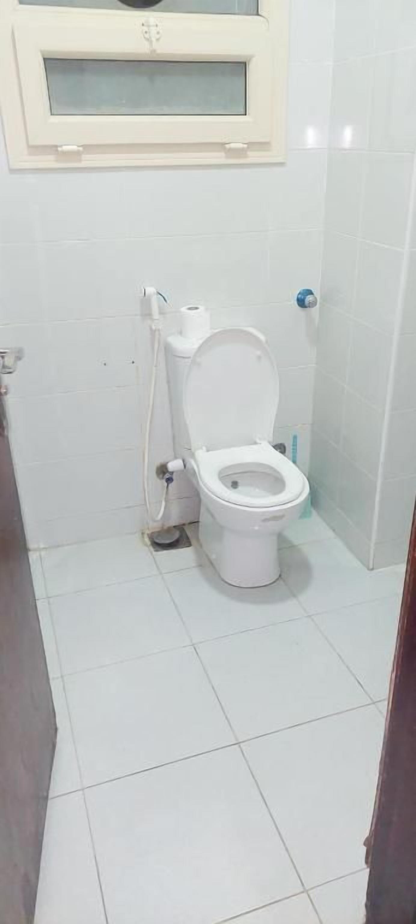 A bathroom with a toilet, a window above it, and a tiled floor.